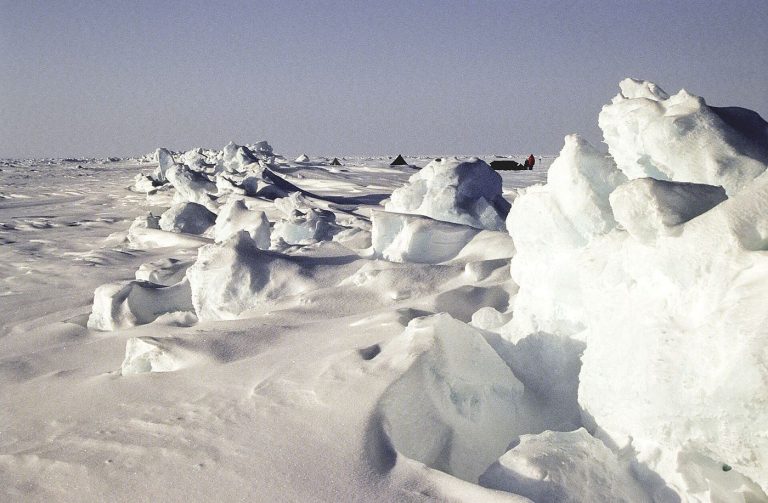 Aerial view of fractured arctic sea ice floating on dark ocean water with melt pools.